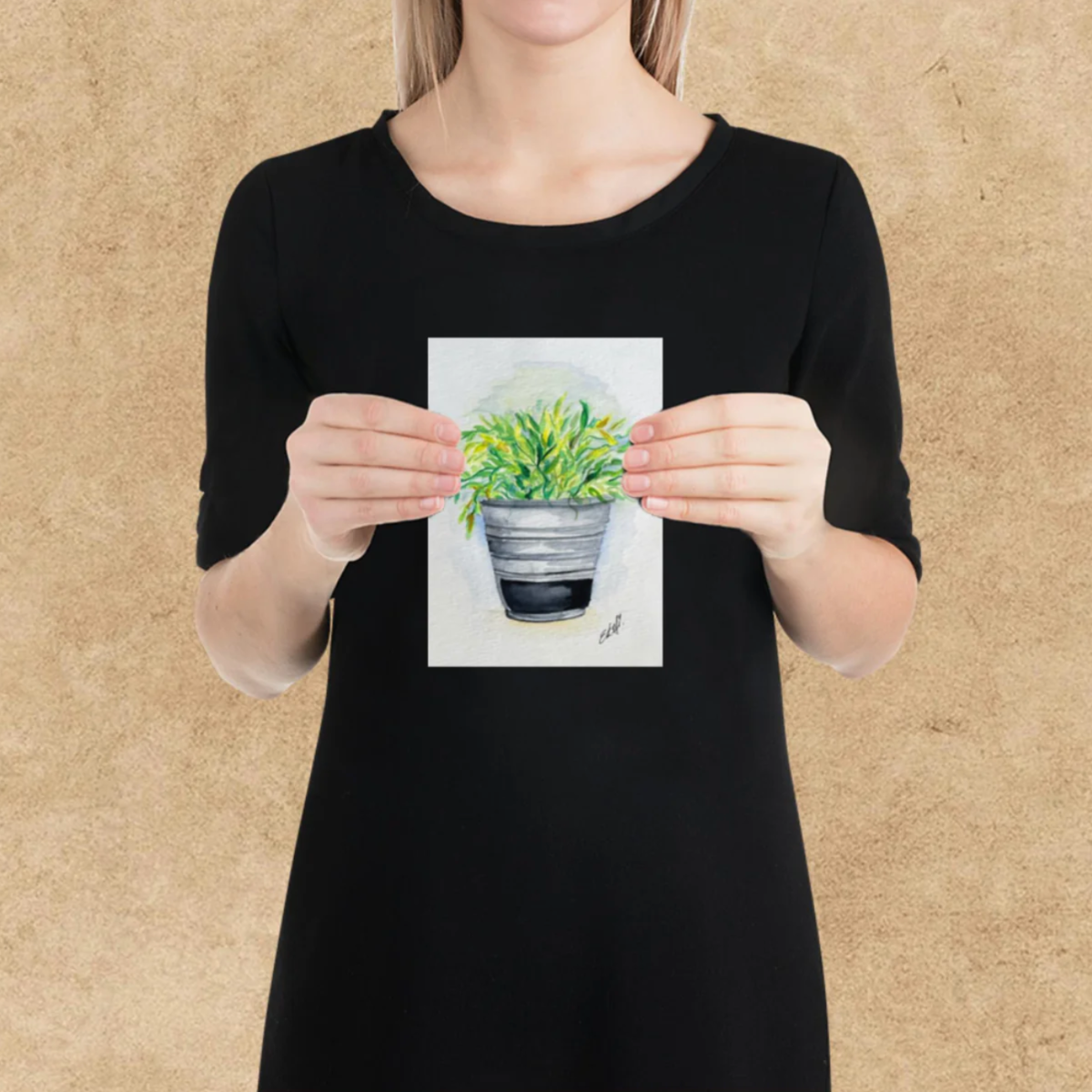 Person holding a small painting of a potted plant against a beige background